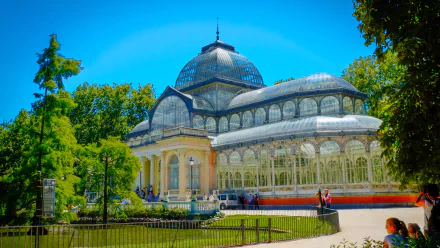 HD desktop wallpaper showcasing the man-made Palacio de Cristal, a stunning glass palace surrounded by lush greenery under a bright blue sky.