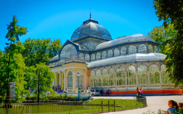HD desktop wallpaper showcasing the man-made Palacio de Cristal, a stunning glass palace surrounded by lush greenery under a bright blue sky.
