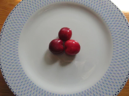 Three vibrant red cherries centered on a white plate with a blue patterned rim, captured in 4K Ultra HD for a crisp PC desktop wallpaper.