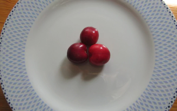 Three vibrant red cherries centered on a white plate with a blue patterned rim, captured in 4K Ultra HD for a crisp PC desktop wallpaper.