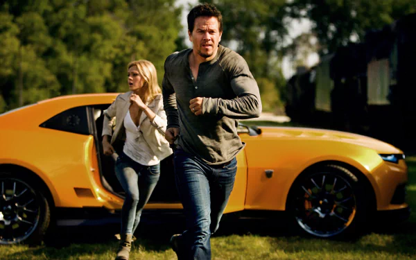 Mark Wahlberg and a woman run away from a yellow car in a scene from *Transformers: Age of Extinction*, showcasing an intense moment from the movie. HD desktop wallpaper.