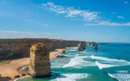 HD desktop wallpaper showcasing the natural coastal rock formations of The Twelve Apostles with clear blue skies and waves crashing along the shore.