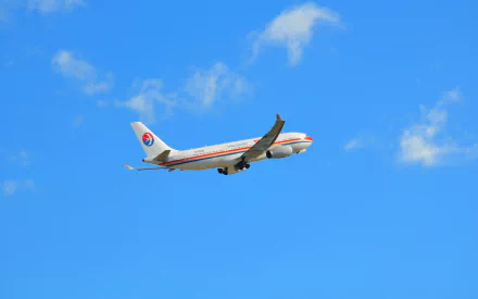 An Airbus A330 passenger plane from China Eastern Airlines soars through a bright blue sky, creating a striking HD desktop wallpaper background.