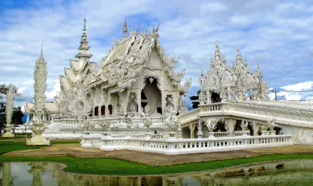 HD wallpaper showcasing the intricate white temple Wat Rong Khun in Chiang Rai, Thailand, reflecting stunning religious architecture against a partly cloudy sky.