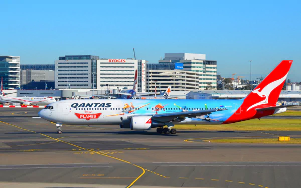 Qantas Boeing 767 airplane with vibrant livery taxis on the runway at Sydney airport against a clear blue sky in this HD desktop wallpaper.