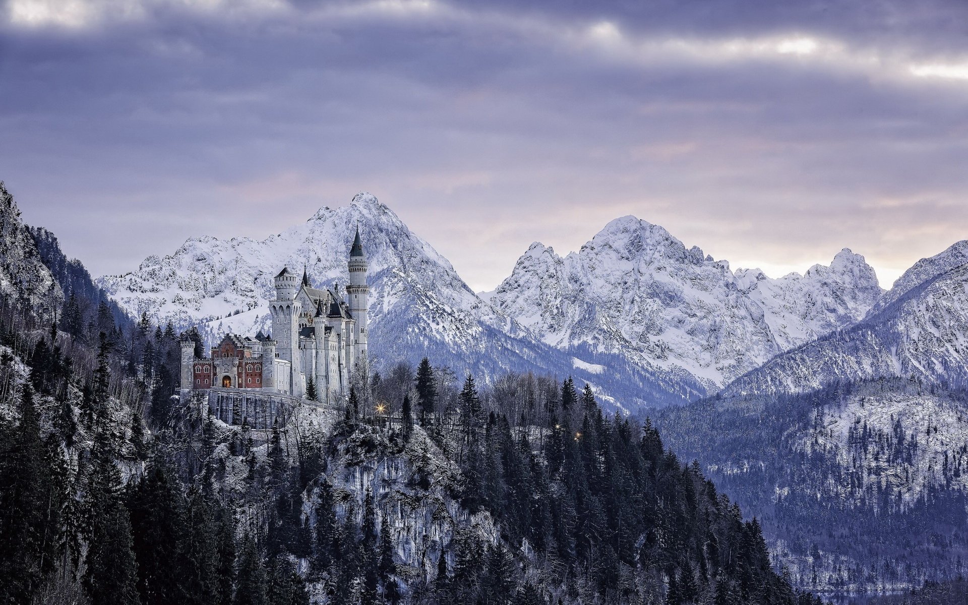 Neuschwanstein Castle, a man-made fairytale palace on a snowy forest ridge beneath rugged alpine peaks and a moody sky — HD PC desktop wallpaper/background