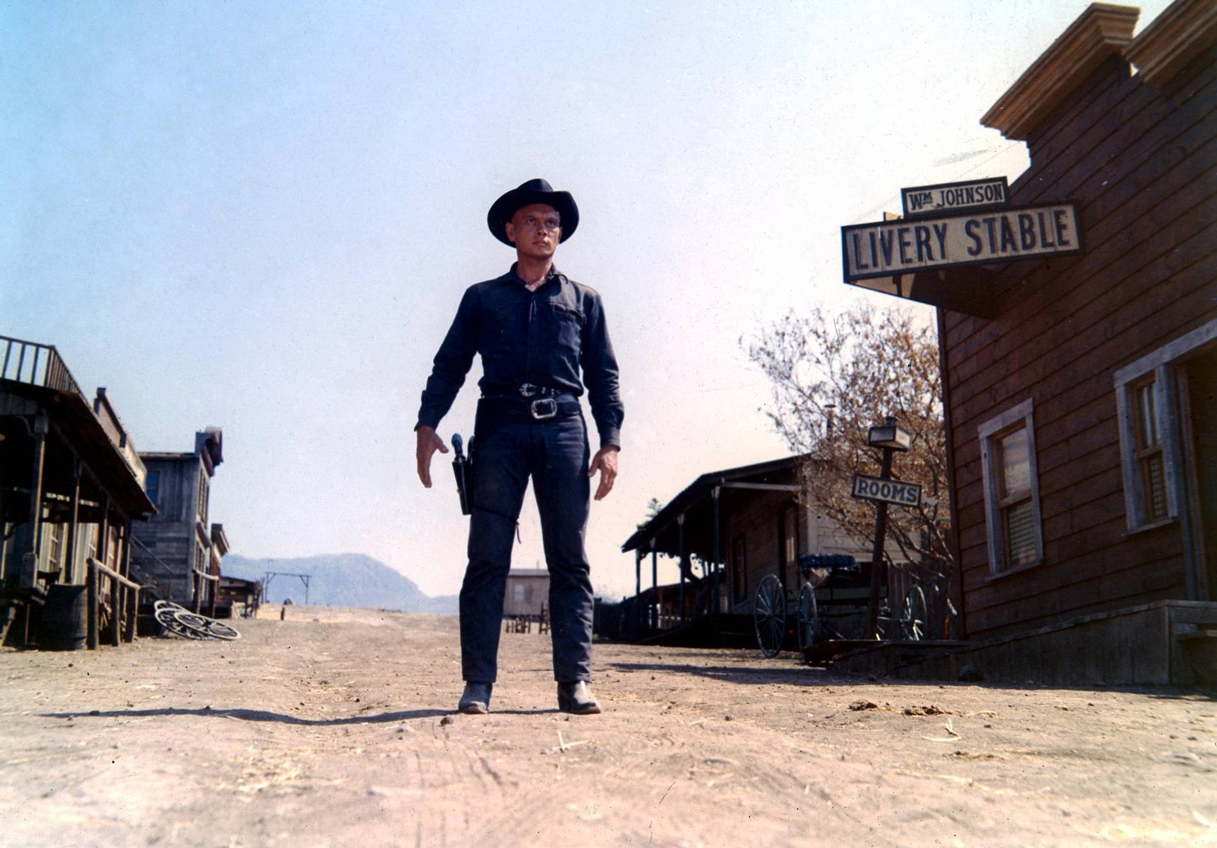 HD PC desktop wallpaper: lone cowboy in black hat and outfit stands in a sunlit, deserted Westworld movie town street.