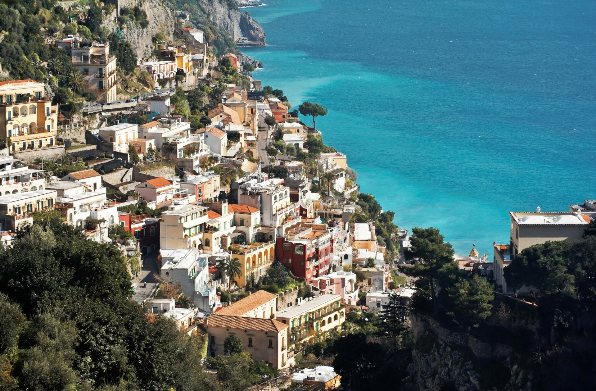 A vibrant coastal view of Amalfi in Salerno, Italy, showcasing colorful cliffside buildings overlooking the bright blue Mediterranean Sea.
