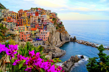 HD wallpaper of Manarola, Cinque Terre, showing colorful houses clustered on rugged cliffs overlooking the sea, with vibrant flowers in the foreground.