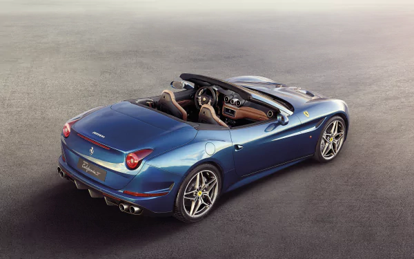 Blue Ferrari California T convertible on textured asphalt, rear three-quarter view — 2K Quad HD PC desktop wallpaper/background.