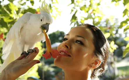 Ukrainian woman Dasha Astafieva interacts with a white cockatoo in a bright outdoor setting, featured in an HD PC desktop wallpaper and background.