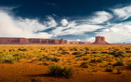 HD PC desktop wallpaper showcasing a scenic desert landscape with red rock formations under a dynamic cloudy sky, capturing the vast beauty of nature.