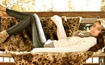 HD desktop wallpaper featuring a woman, tagged as Taylor Marie Hill, lounging on a leopard-print blanket, wearing a white sweater, jeans, and boots, with a serene forest backdrop.