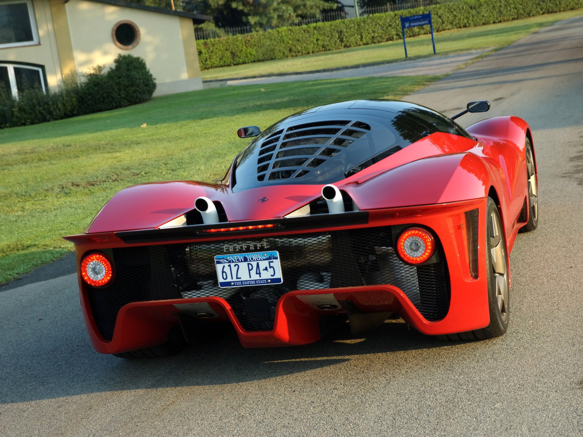 Red Ferrari Pininfarina P4/5 concept vehicle, rear three-quarter view on a sunlit road — HD PC desktop wallpaper background.