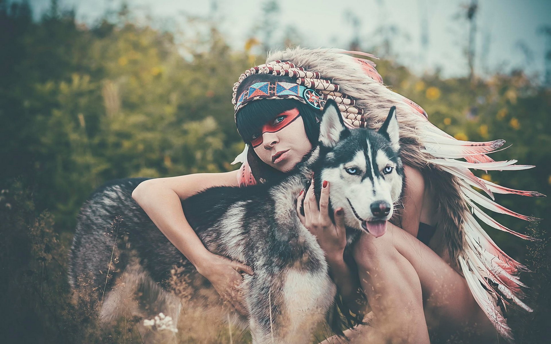 A stunning HD desktop wallpaper featuring a husky dog and a young woman in Native American-inspired attire, capturing a serene moment in nature among lush greenery.