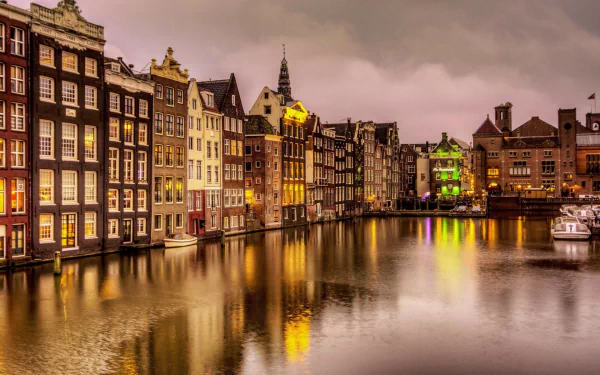 HD desktop wallpaper of Amsterdam's man-made canal houses reflected in calm water under a moody sky.