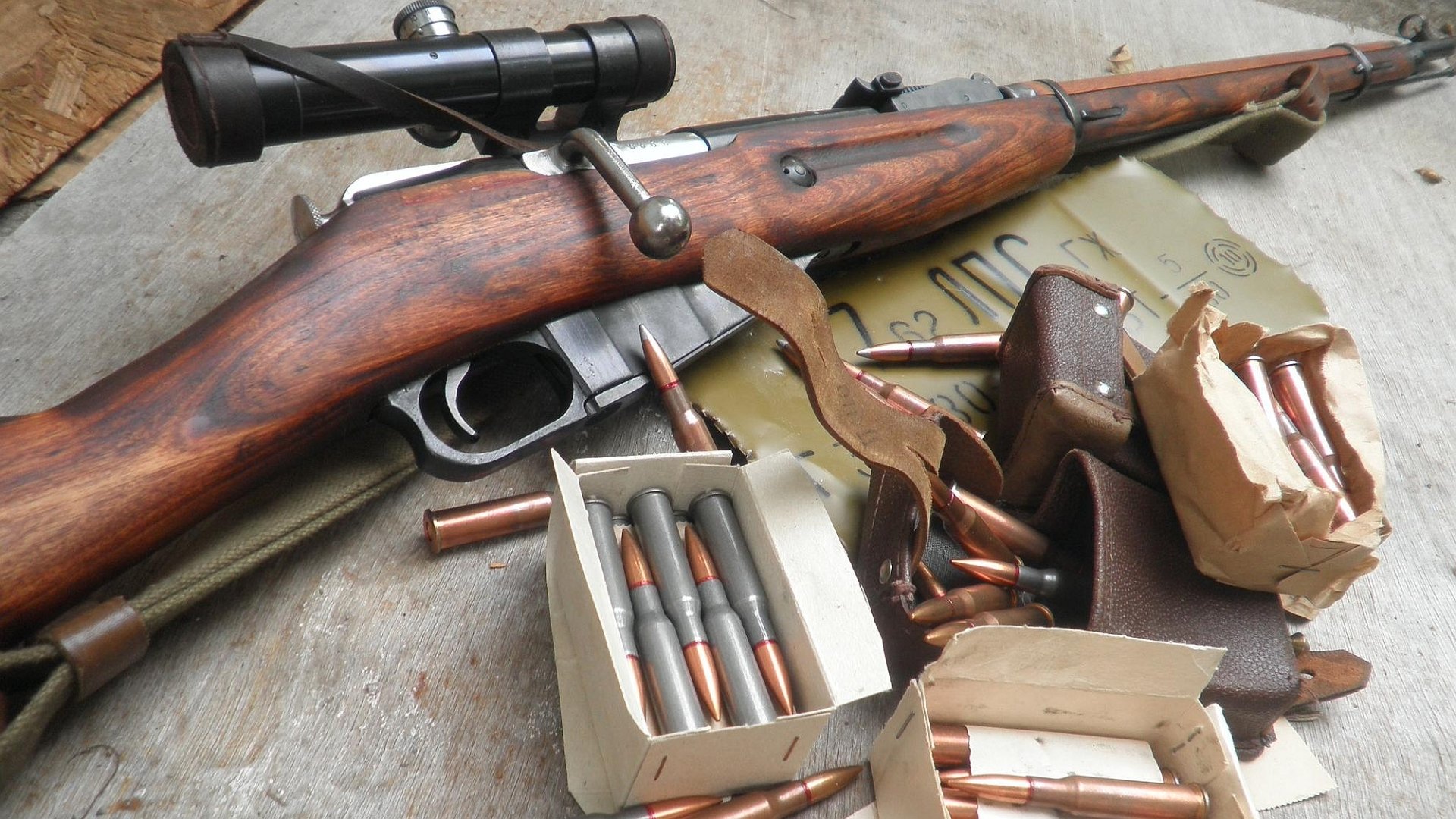 HD PC desktop wallpaper/background showing a man-made Mosin Nagant rifle with scope, boxes of ammunition and loose rounds arranged on a weathered surface.
