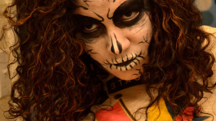 Artistic sugar skull portrait with blacked eyes and stitched-mouth makeup, wild curly hair framing the face — 2K Quad HD PC desktop wallpaper and background.
