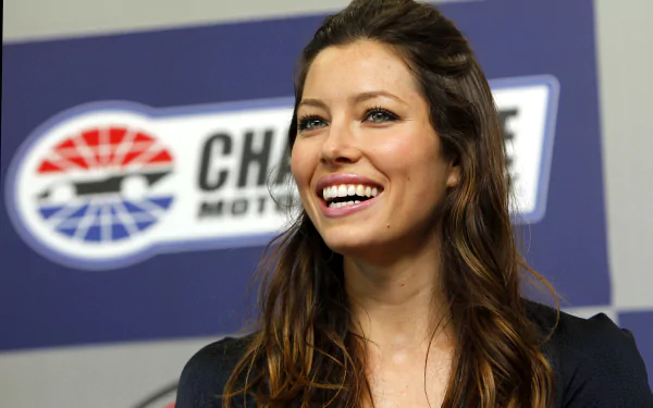 Smiling female celebrity with long brown hair against a motorsport logo backdrop — 4K Ultra HD PC desktop wallpaper/background.