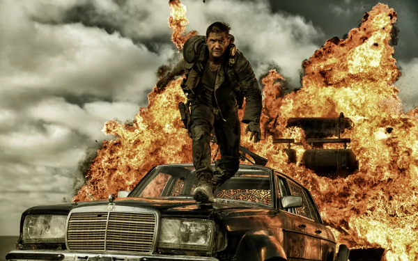 Max Rockatansky, portrayed by Tom Hardy, stands on a car against a backdrop of explosions in this intense scene from *Mad Max: Fury Road*, captured in stunning 4K Ultra HD.