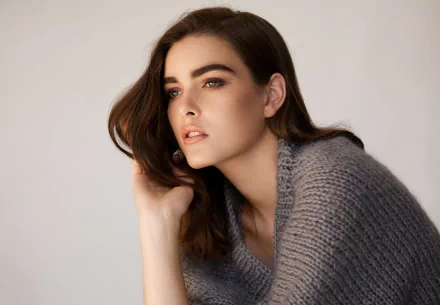 HD PC desktop wallpaper of a celebrity model in a gray knit sweater, gazing off-camera with soft lighting and tousled dark hair.