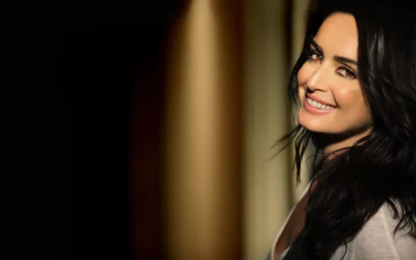 A vibrant HD wallpaper featuring actress Ana de la Reguera, showcasing her radiant smile against a softly lit background, perfect for enhancing any desktop setup.