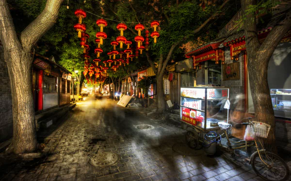 A vibrant nighttime scene from Beijing featuring a narrow street adorned with red lanterns, trees, and a food stall, showcasing the charm of man-made beauty in China.