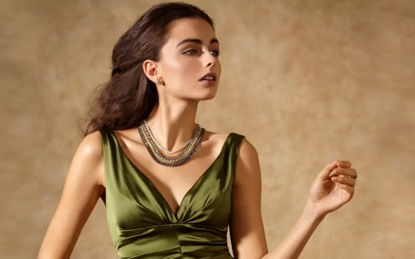 HD PC desktop wallpaper of a woman model in an olive-green dress wearing layered necklaces, posed gracefully against a warm, textured backdrop.