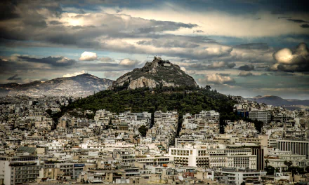 Night view of Athens, Greece, showcasing the illuminated cityscape and the prominent hill under dramatic clouds in 4K Ultra HD quality.
