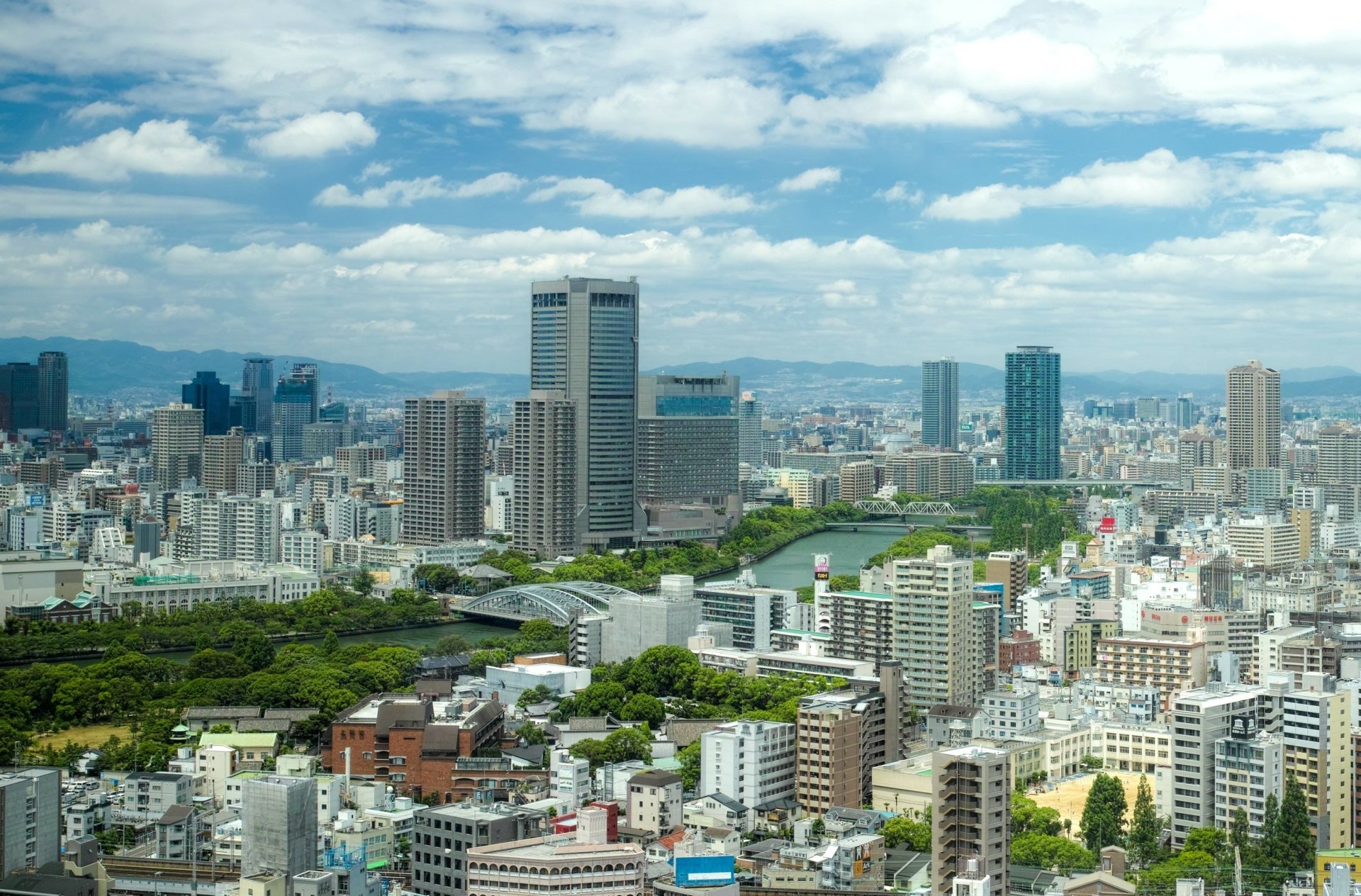 HD desktop wallpaper showcasing a panoramic view of Osaka, Japan, featuring its man-made urban landscape under a partly cloudy sky.