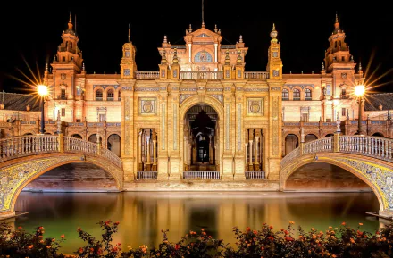 A stunning view of Plaza de España in Seville, Spain, featuring illuminated architecture and a serene water reflection, creating an enchanting night scene.