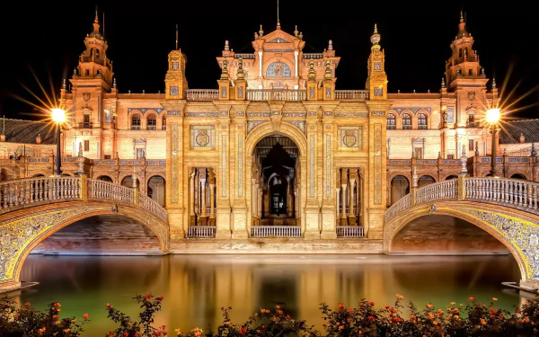 A stunning view of Plaza de España in Seville, Spain, featuring illuminated architecture and a serene water reflection, creating an enchanting night scene.
