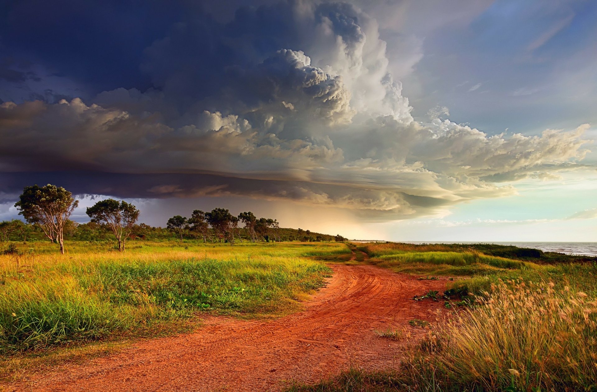 A scenic seashore road winds through lush greenery beneath dramatic storm clouds, capturing the beauty of nature in a breathtaking HD desktop wallpaper.
