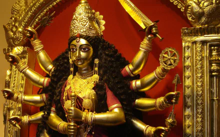 HD wallpaper featuring a detailed depiction of Goddess Durga, a prominent figure in Hinduism, with multiple arms holding various weapons, set against a rich red and gold background.