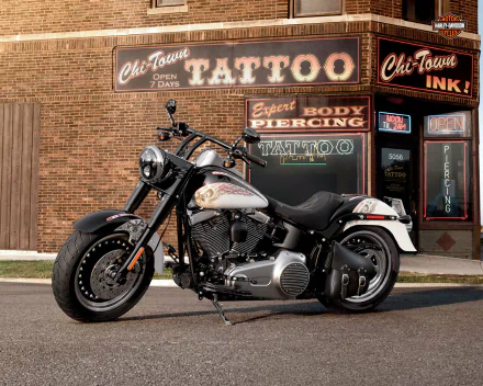 Harley-Davidson Fat Boy motorcycle parked in front of a brick building with tattoo and piercing shop signs, captured as an HD PC desktop wallpaper and background.