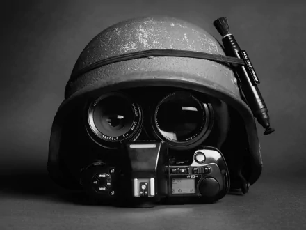 Black and white HD desktop wallpaper showing a Nikon camera with lenses arranged inside a worn helmet against a dark background.