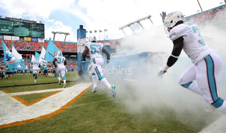 HD PC desktop wallpaper featuring Miami Dolphins players entering the stadium through smoke, capturing the energy and spirit of the team in a vibrant sports scene.