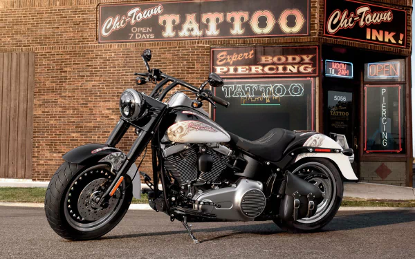 Harley-Davidson Fat Boy motorcycle parked in front of a brick building with tattoo and piercing shop signs, captured as an HD PC desktop wallpaper and background.