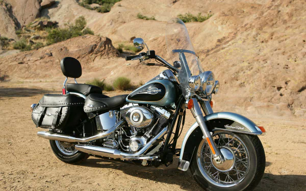 Harley-Davidson Heritage Softail motorcycle bike vehicle with chrome accents and leather saddlebags parked by rocky desert hills, HD desktop wallpaper.