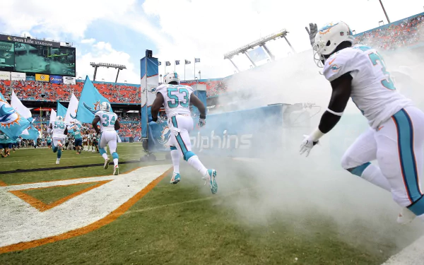 HD PC desktop wallpaper featuring Miami Dolphins players entering the stadium through smoke, capturing the energy and spirit of the team in a vibrant sports scene.