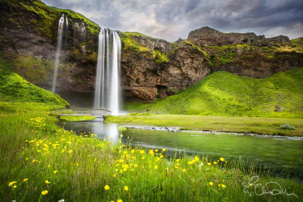 HD desktop wallpaper of a vibrant green landscape featuring a cascading waterfall surrounded by lush hills and wildflowers under a cloudy sky.