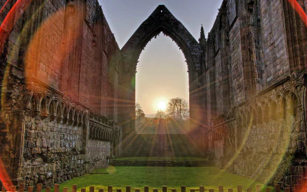 Sunset shines through the ancient archway of Bolton Priory, highlighting the stone walls in this HD man-made structure desktop wallpaper.