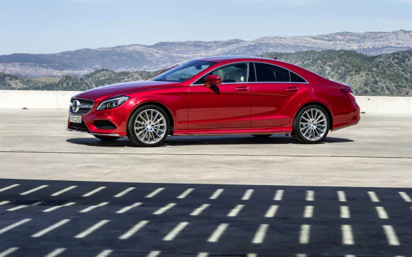 Red Mercedes‑Benz CLS‑Class sedan on sunlit pavement with mountains in the distance — 4K Ultra HD PC desktop wallpaper showcasing the Mercedes‑Benz vehicle.