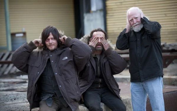 Three characters from The Walking Dead—Hershel Greene, Rick Grimes, and Daryl Dixon—pose playfully, with one covering his eyes and the others covering their ears, set in a dramatic backdrop.