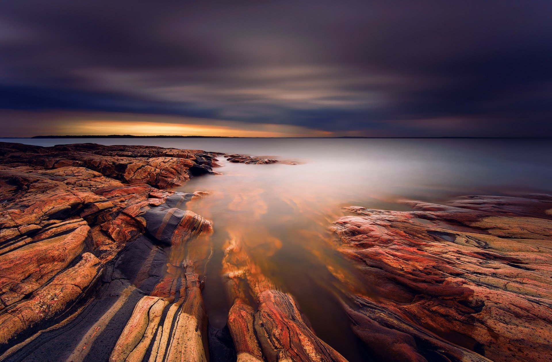 HD PC desktop wallpaper showing dramatic clouds over a tranquil sea and rocky seashore, vivid nature colors reflected in smooth, glassy water.