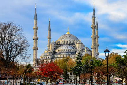 A stunning view of the Sultan Ahmed Mosque in Istanbul, Turkey, showcasing its iconic architecture and surrounding vibrant trees against a beautifully cloudy sky.