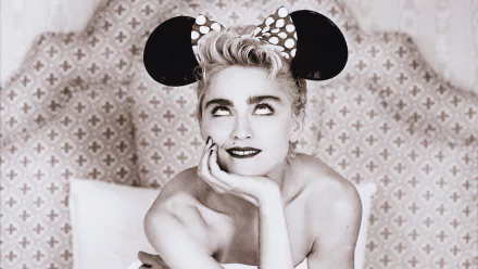 A black-and-white HD wallpaper featuring Madonna wearing a polka-dot Mickey Mouse headband, playfully posing with a thoughtful expression against a stylish backdrop.