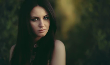 HD desktop wallpaper featuring a woman with long dark hair, exuding a contemplative mood against a blurred natural background.