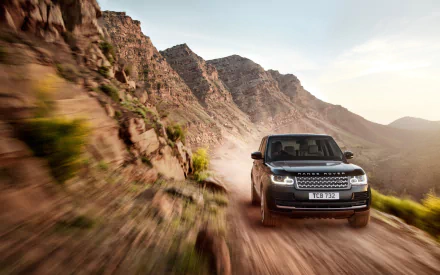 HD PC desktop wallpaper: black Range Rover vehicle driving on a dusty mountain road, off-road motion kicking up dust against rugged canyon cliffs.