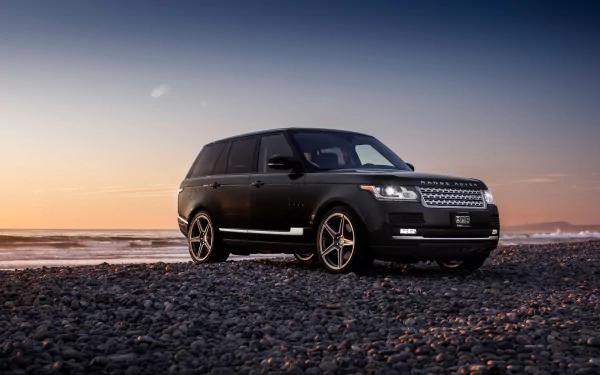 A sleek black Range Rover parked on a rocky beach at sunset, captured in high definition for a stunning desktop wallpaper.